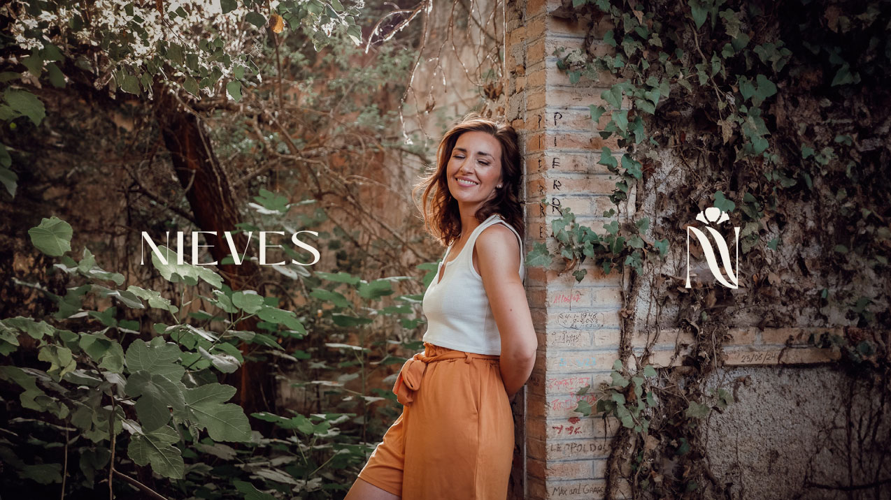 Nieves Espigares sonriendo, apoyada en un muro cubierto de hiedra en un jardín